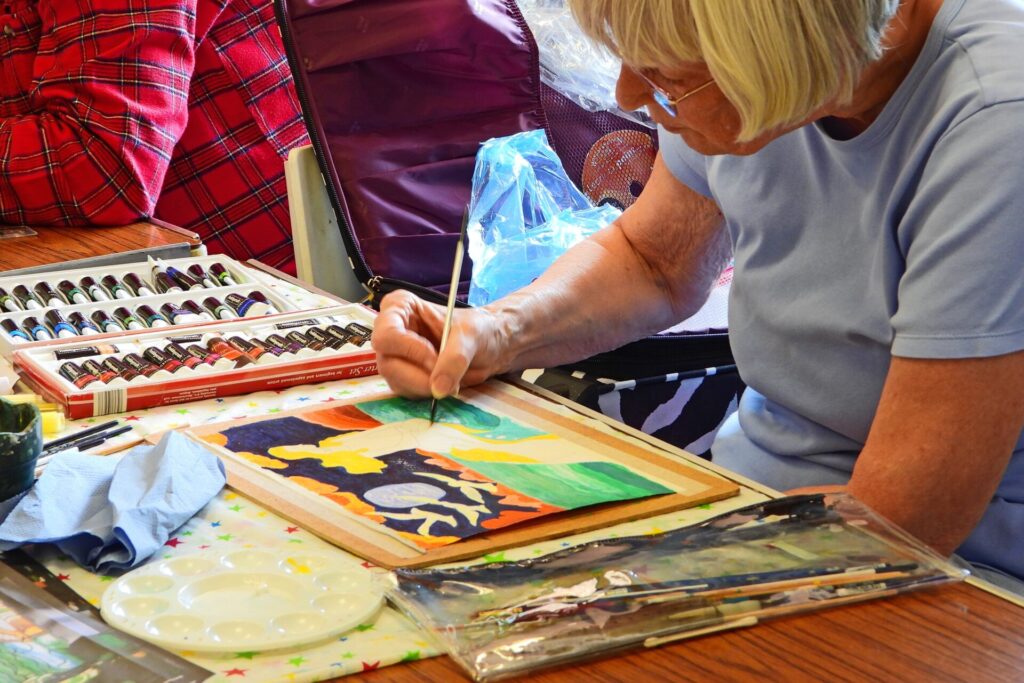Painter completing her piece with her paints, brushes and palette within reach.