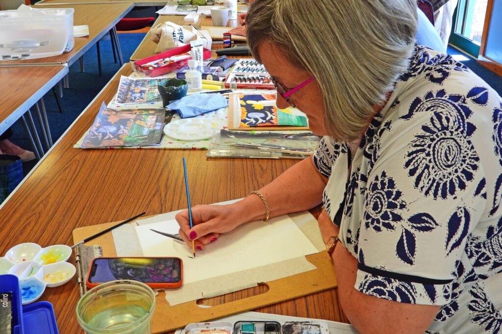 Artist surrounded by her paints starting to work an new piece, using an image on her phone for reference.