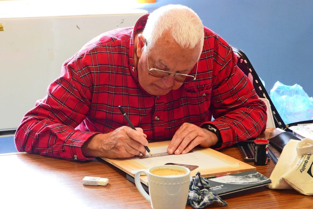 Man using pencil and rule to map out his drawing with a cup of coffee near by.