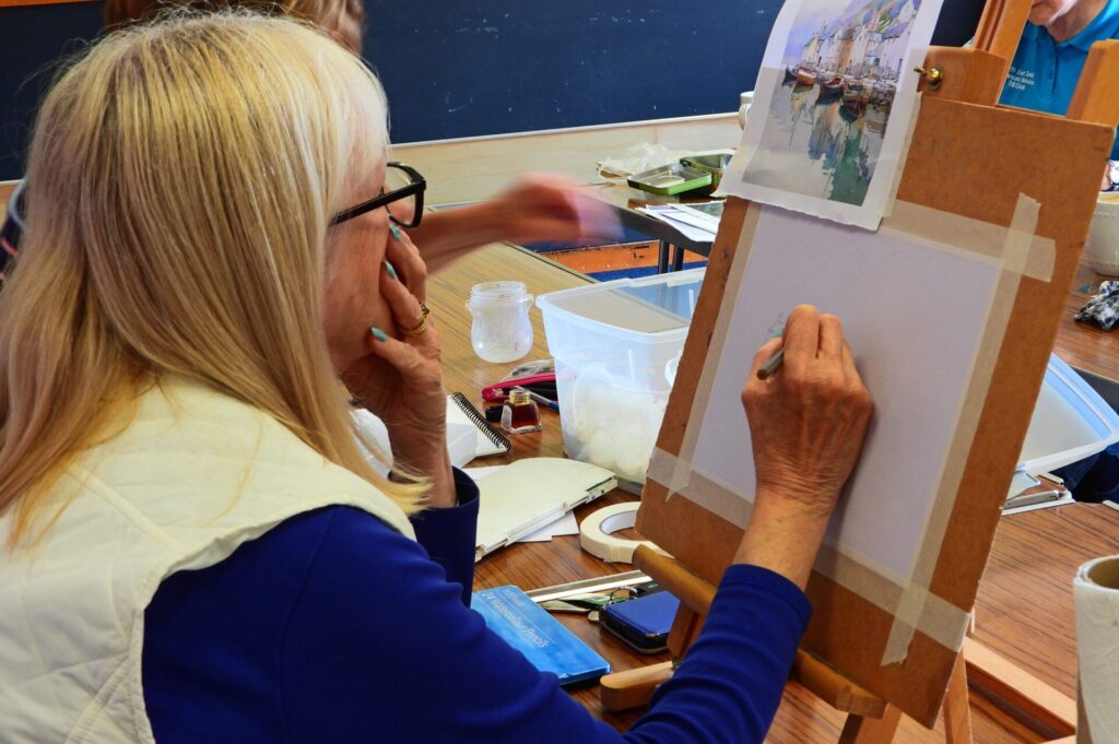 Group member starting to draw a piece on an easel copying from an existing picture, surrounded by her artist tools