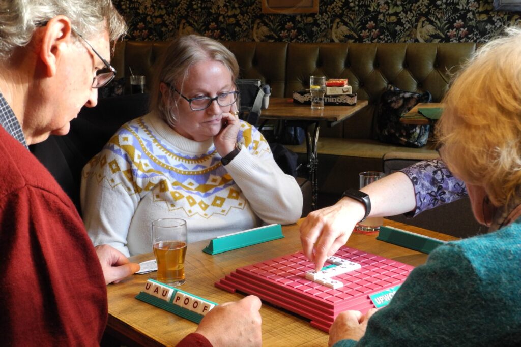 Four players after the game Upwords has started, one is about to place tiles to make a word.
