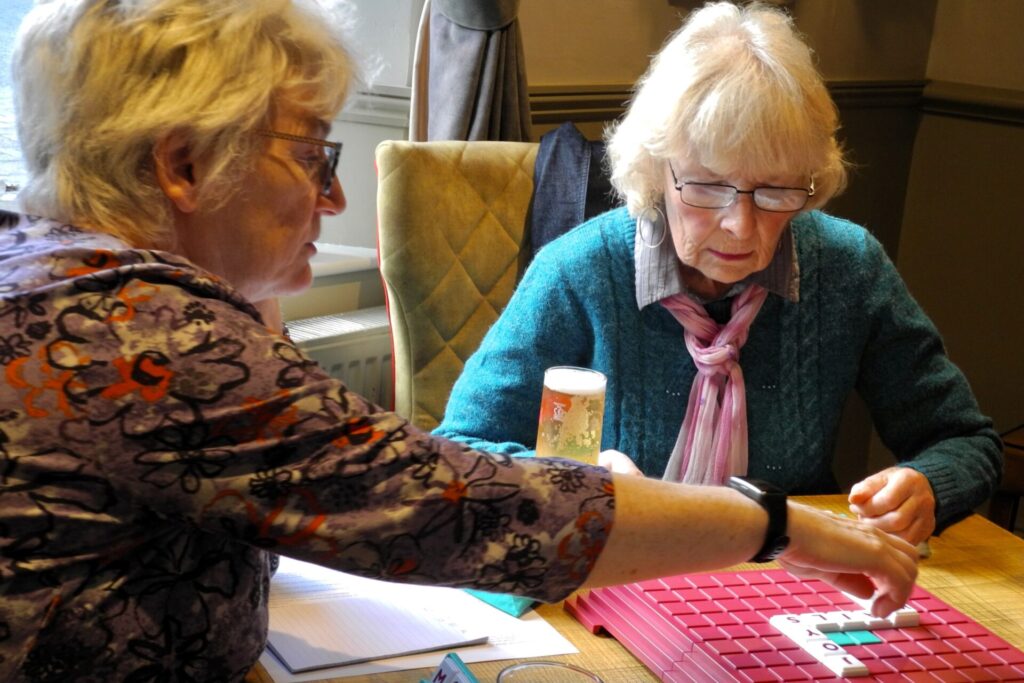 Two players looking at the Upwords board, one with hand stretched out to place a word.